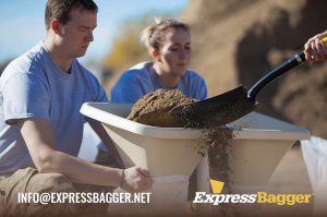 Man and woman using the ExpressBagger Classic sandbag filling station tool to fill sandbags while a third man shovels sand